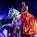 Un cavaliere in costume tipo akama rosso su un cavallo grigio che fa il passo spagnolo, durante uno spettacolo equestre illuminato da luci viola e verdi, e un fumo leggere sullo sfondo