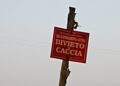 Cartello rosso di divieto di caccia della Provincia di Macerata, relativo a una zona di ripopolamento e cattura, fissato a un palo di legno
