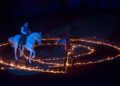 Cavallo bianco montato da un cavaliere durante uno spettacolo equestre notturno, all'interno di un cerchio di fuoco